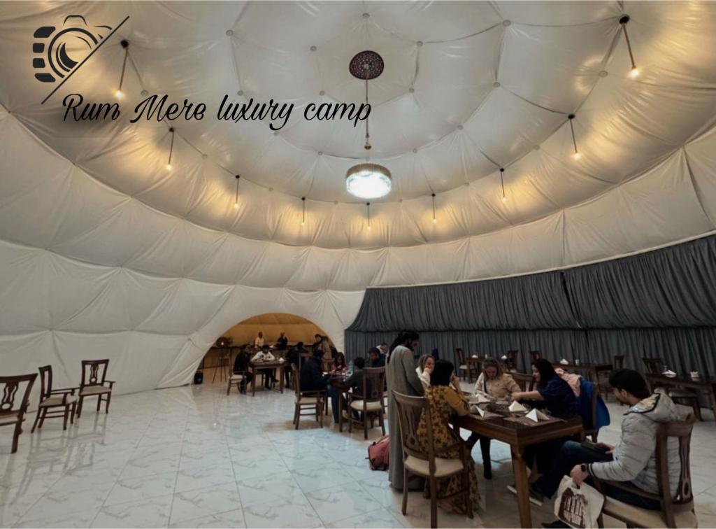 Una tienda blanca con gente sentada en mesas. en Rum Mere luxury camp, en Wadi Rum