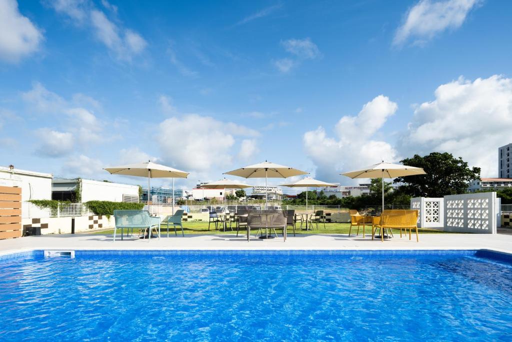 una piscina con sombrillas, mesas y sillas en ネストホテル石垣マエサトビーチ en Isla Ishigaki