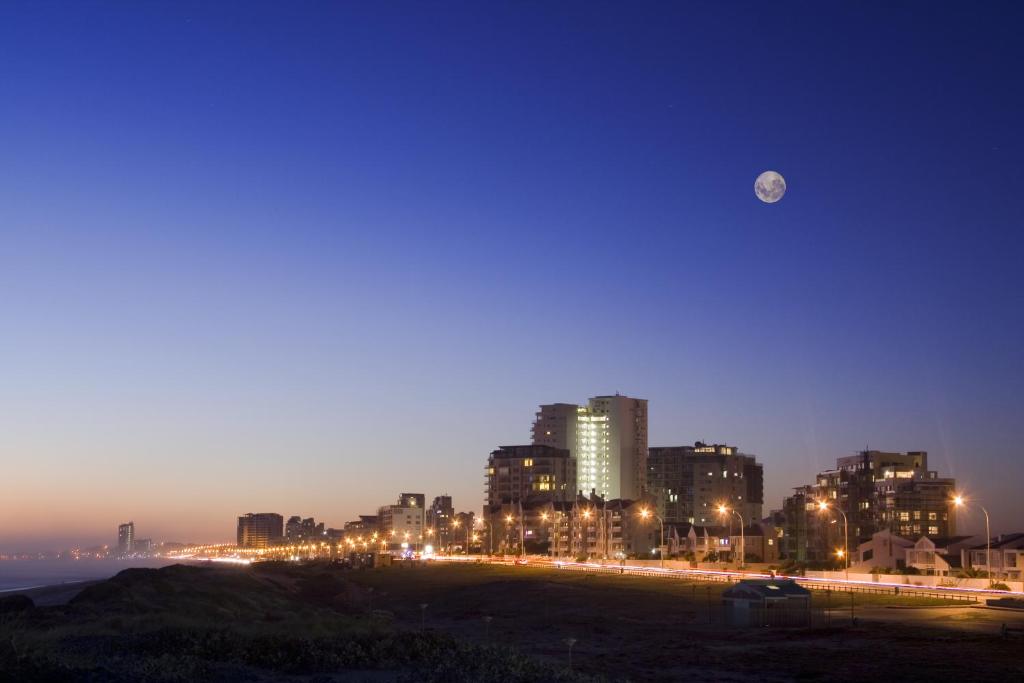 a city at night with the moon in the sky at Cape Town Beachfront Accommodation in Blouberg in Bloubergstrand
