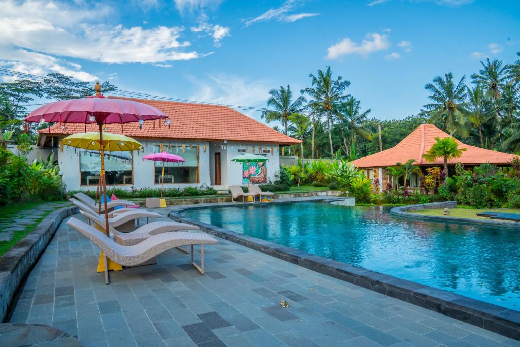 een zwembad van het resort met stoelen en een parasol bij Kampung Uma Dawa Villas and Spa in Ubud