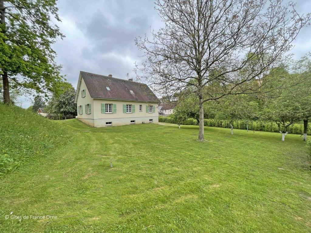 a house on a grassy hill with a tree at Maison confortable dans le Perche avec jardin et animaux admis - FR-1-497-205 in Longny-au-Perche