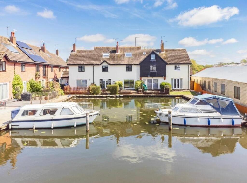 dois barcos estão ancorados na água perto de casas em Cottage On The Quay em Wroxham