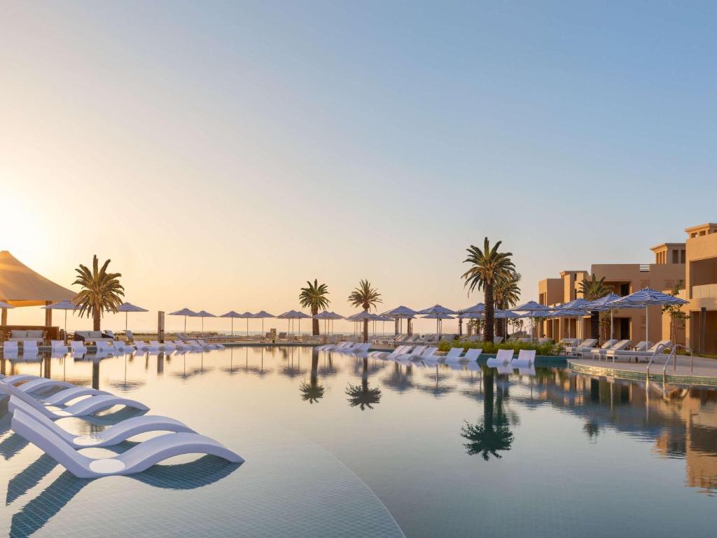 a pool at a resort with chairs and palm trees at Sofitel Al Hamra Beach Resort in Ras al Khaimah