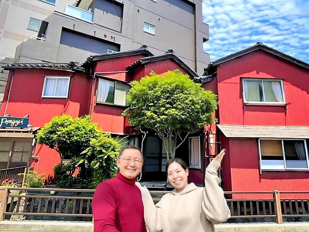Ein Mann und eine Frau stehen vor einem roten Haus. in der Unterkunft Guest House Pongyi in Kanazawa