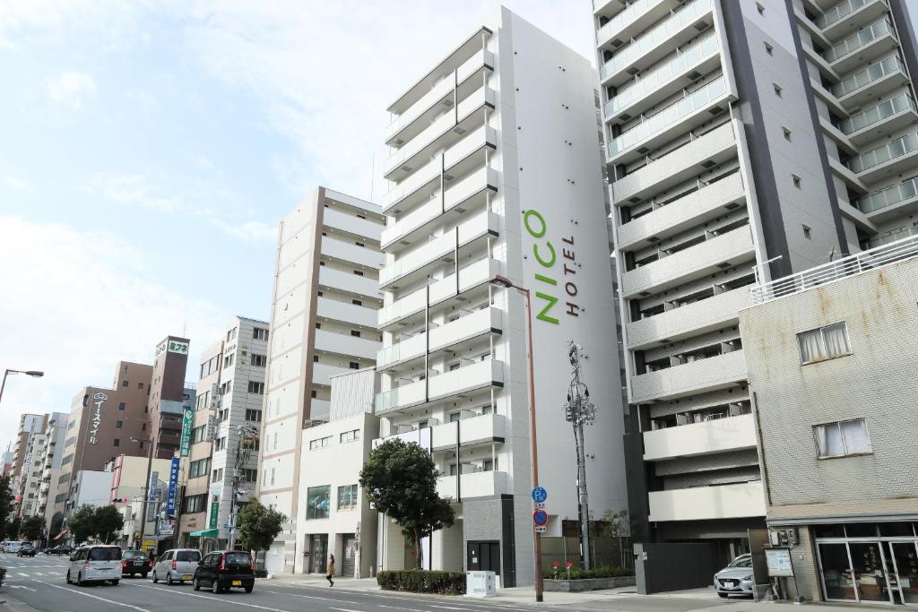 ein hohes weißes Gebäude in einer Stadtstraße mit Autos in der Unterkunft Nico Hotel in Osaka