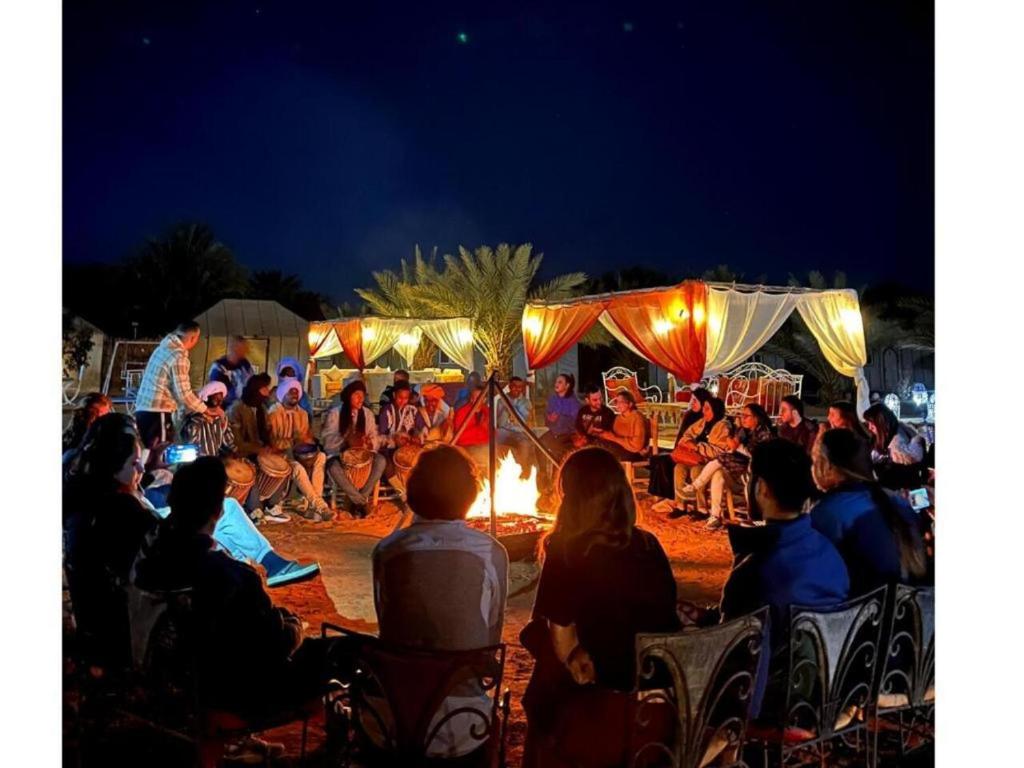 a crowd of people sitting around a fire at night at Merzouga Top Desert Camp in Merzouga