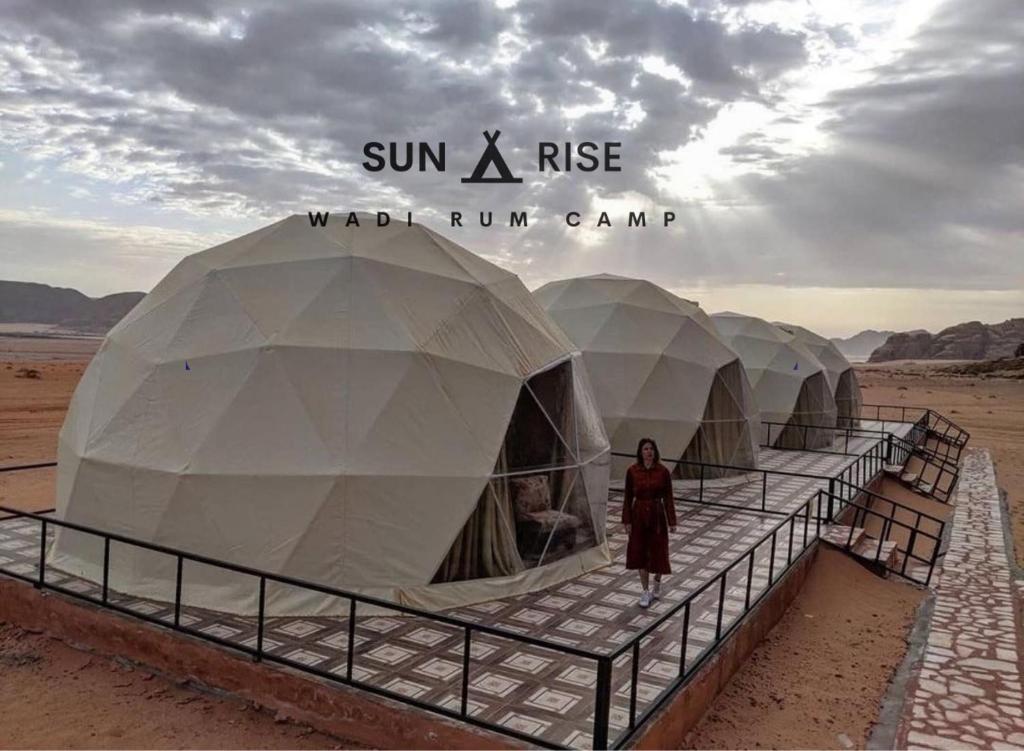 瓦迪拉姆的住宿－Sunrise Wadi Rum Camp，站在沙漠中一排帐篷前面的女人