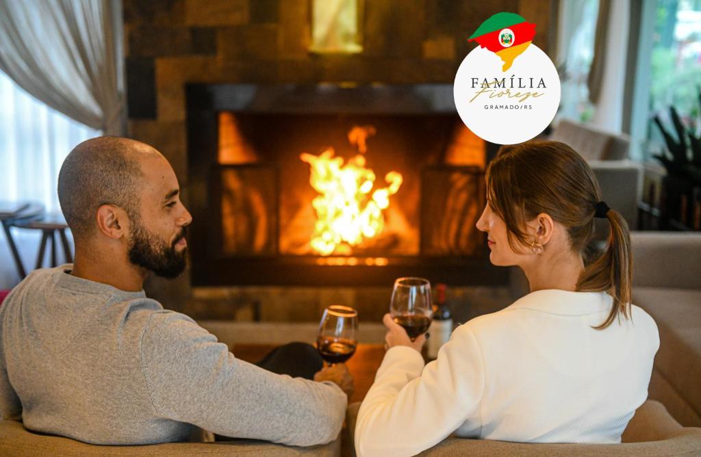 un hombre y una mujer bebiendo vino frente a una chimenea en Hotel Fioreze Primo, en Gramado