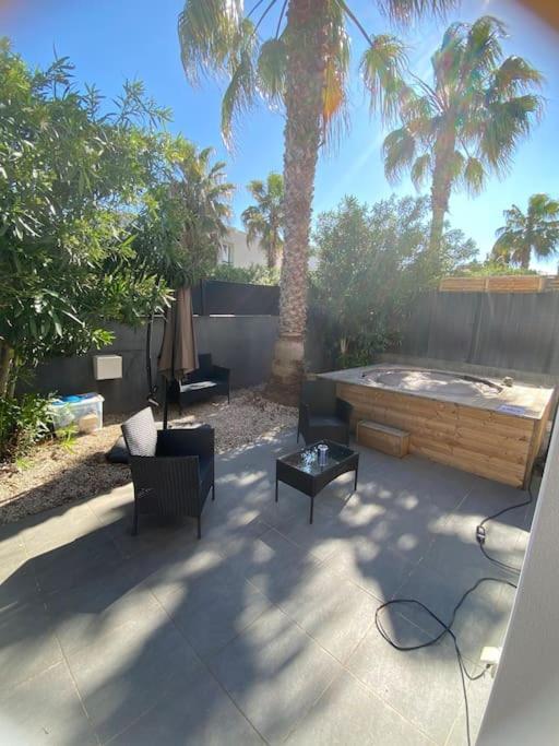 une terrasse avec un bain à remous, des chaises et des palmiers dans l'établissement Villa avec jacuzzi - 3 chambres, à Béziers