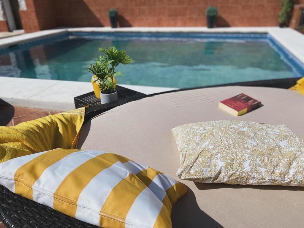 una mesa con una almohada y un libro junto a una piscina en Hevres El Capricho en Málaga