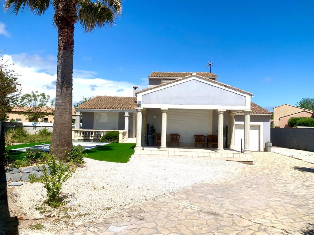 une maison blanche avec un palmier devant dans l'établissement grande villa piscine Marseillan plage cap agde, à Marseillan