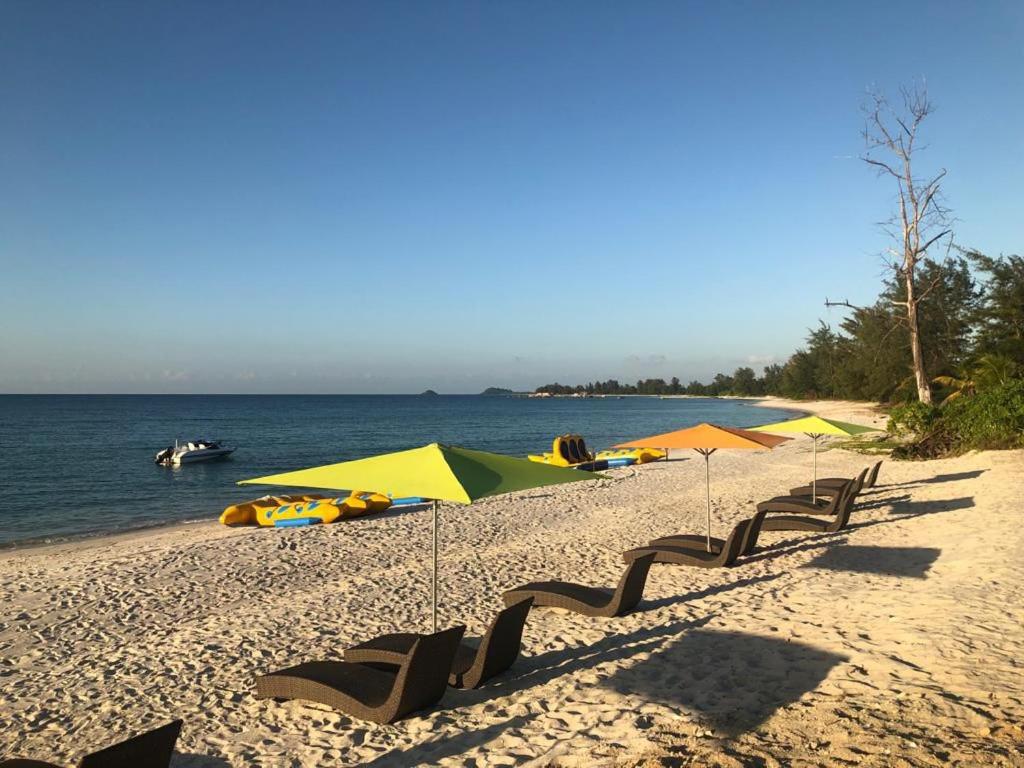 einen Strand mit Stühlen und Sonnenschirmen und dem Wasser in der Unterkunft New Belitung Holiday Resort in Pasarbaru