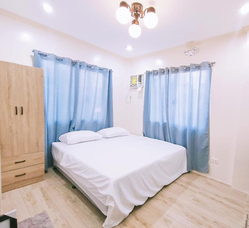 a bedroom with blue curtains and a white bed at Intoy's Place in Panglao