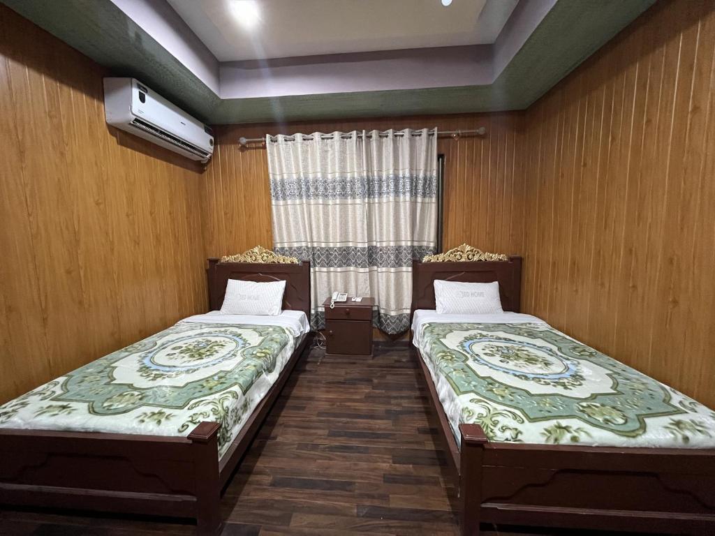 two beds in a room with wooden walls and a window at Blue Sky Hotel & Restaurant in Skardu