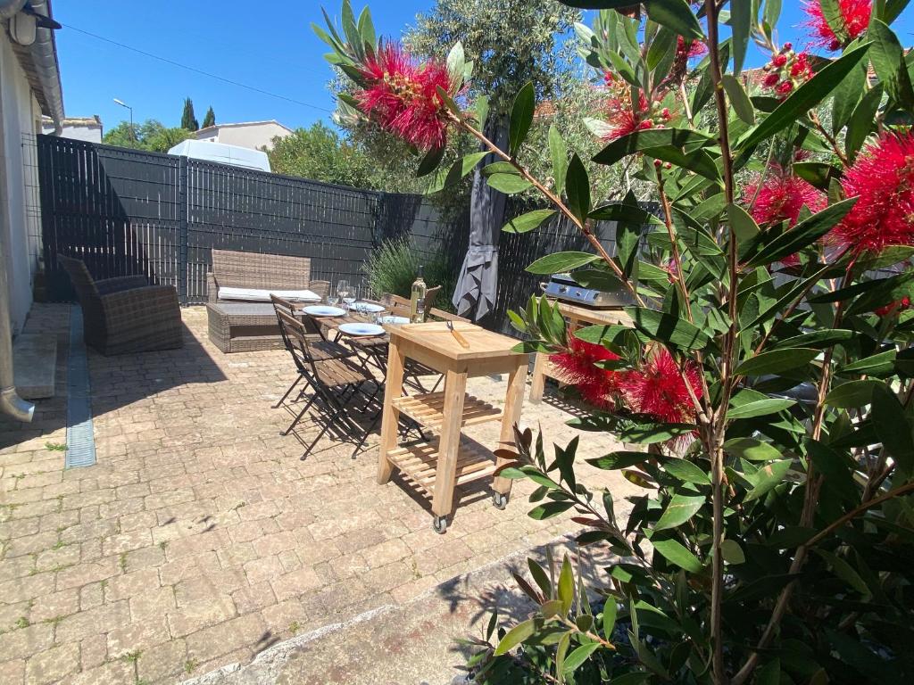 een patio met een tafel en een bos met rode bloemen bij Gîte indépendant en centre-ville in LʼIsle-sur-la-Sorgue