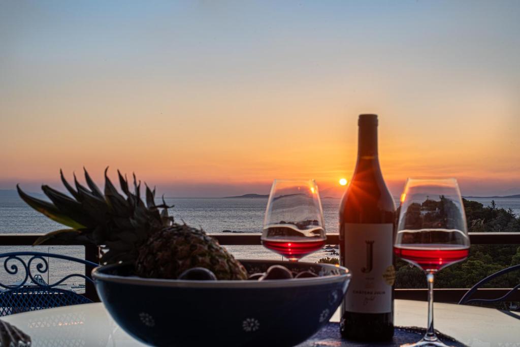 a table with two glasses of wine and a bowl of pineapple at Feliz Apt- Breathtaking Seaview and Sunset by ΜΡS in Anavyssos