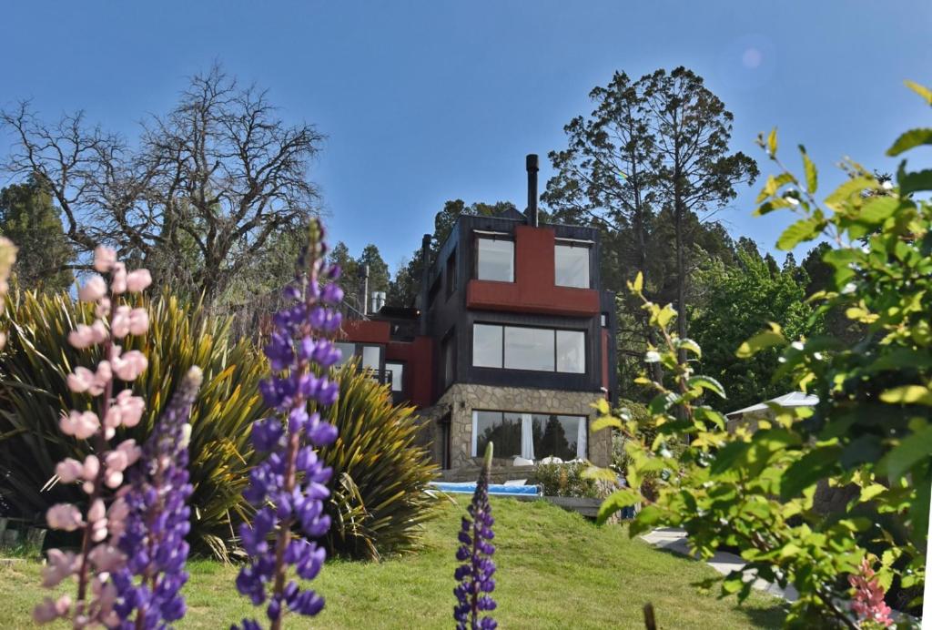 une maison sur une colline avec des fleurs devant elle dans l'établissement Rosas Blancas Apart Hotel By Visionnaire, à San Martín de los Andes