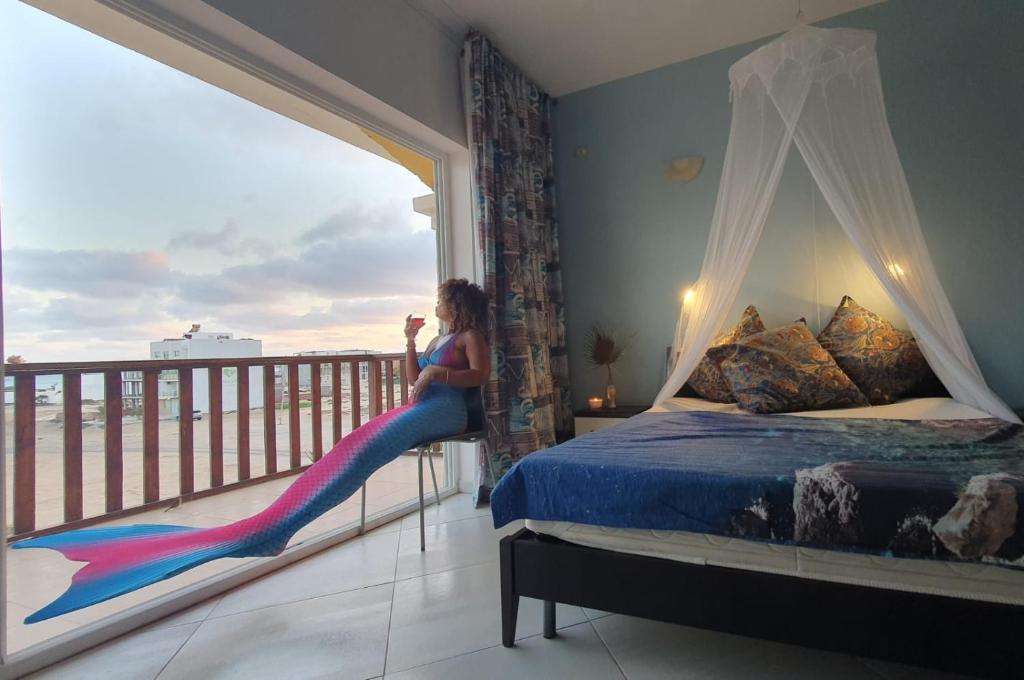 una mujer sentada en una cama mirando por una ventana en EMPFEHLUNG der MEERJUNGFRAU, en Sal Rei