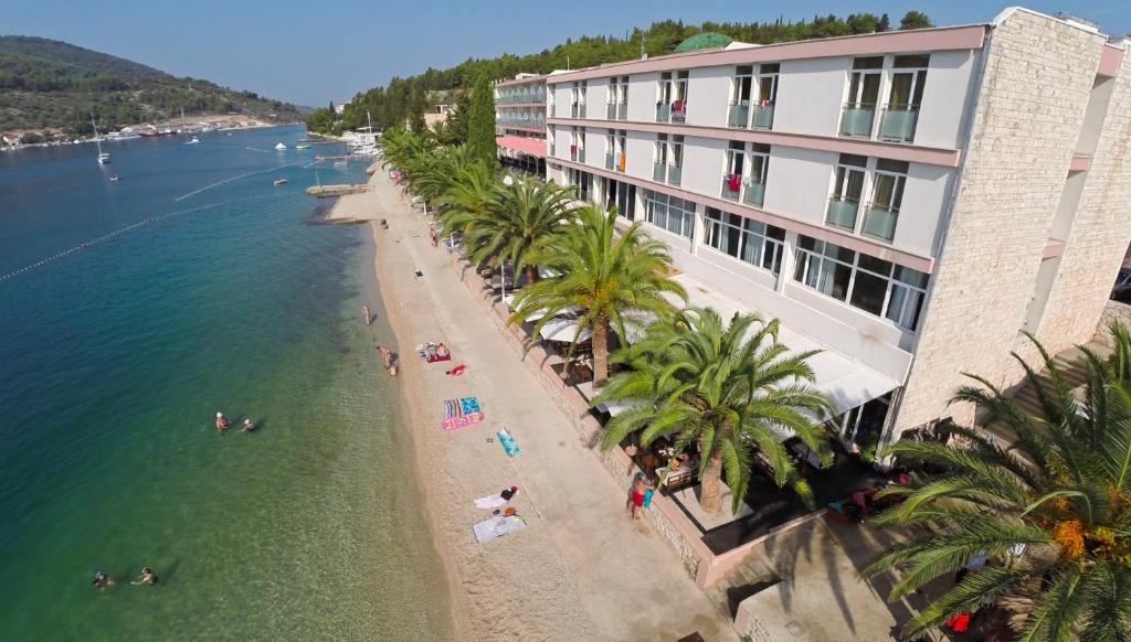 a view of a beach with palm trees and a building at Hotel Posejdon Vela Luka in Vela Luka