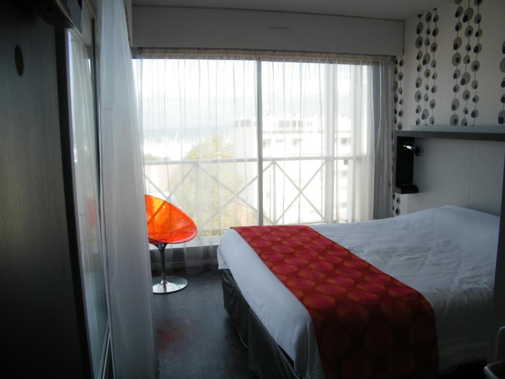 a bedroom with a bed and a window with a red chair at Hôtel Le Nautic in Arcachon