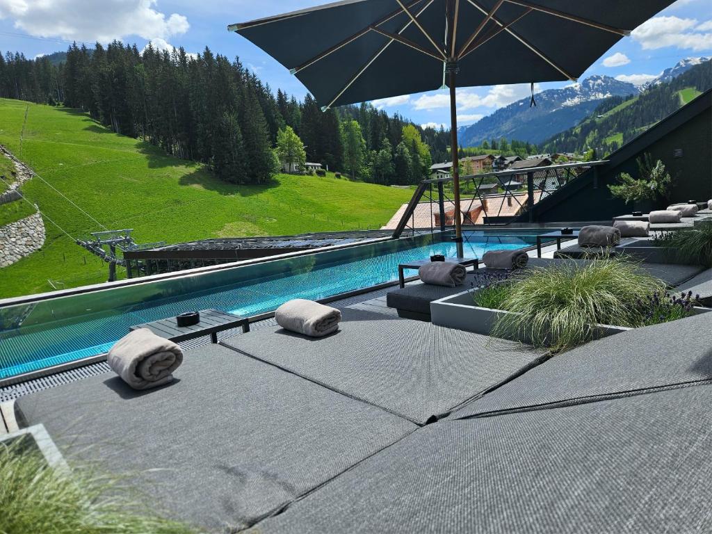 a swimming pool with an umbrella and some chairs at ALMMONTE PRÄCLARUM SUITES Design Hotel in Wagrain