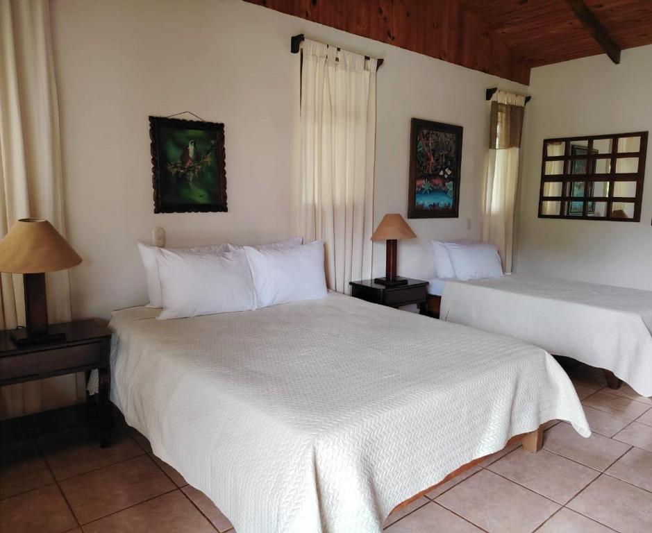 duas camas num quarto com lençóis brancos e candeeiros em Hotel Cacao Río Celeste em Bijagua