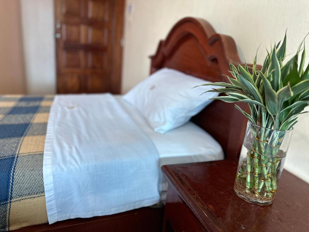 1 dormitorio con 1 cama con un jarrón sobre una mesa en Kanoas Hostal, en Puyo