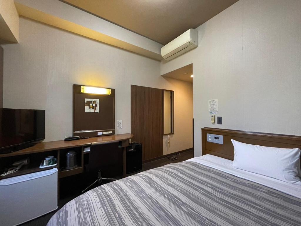 Hotel Route-Inn Fukui Ekimae في فوكوي: غرفة فندقية بسرير وتلفزيون بشاشة مسطحة