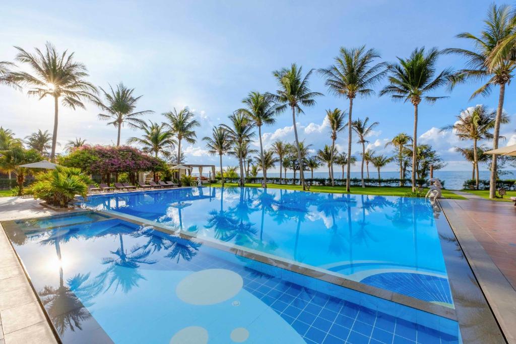 a large swimming pool with palm trees in the background at Sunny Beach Resort & Spa in Mui Ne