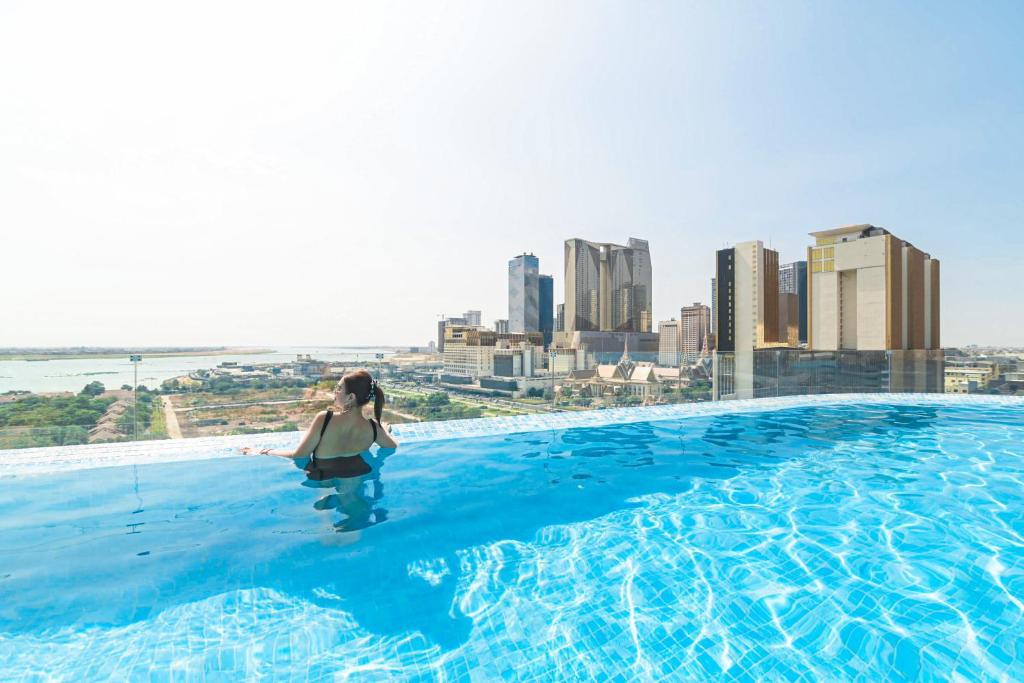 a woman standing on the edge of a swimming pool with a city skyline at Chaiya Palace Hotel in Phnom Penh