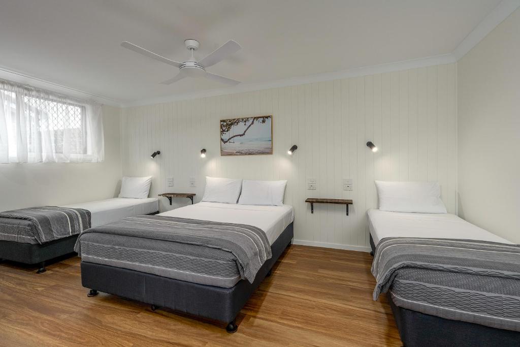 three beds in a room with white walls and wood floors at Coast Inn Motel in Ballina