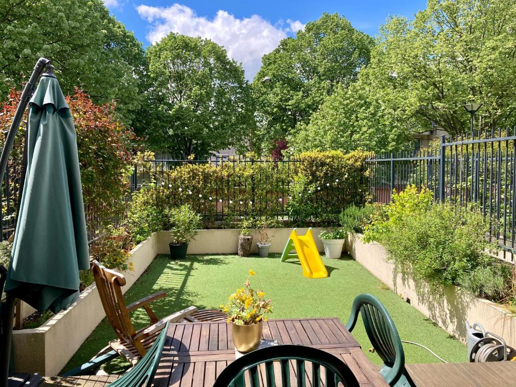 une terrasse avec une table, un parasol et une aire de jeux dans l'établissement Loft 3 pieces sur jardin - 15 minutes de Paris avec parking, à Bagneux