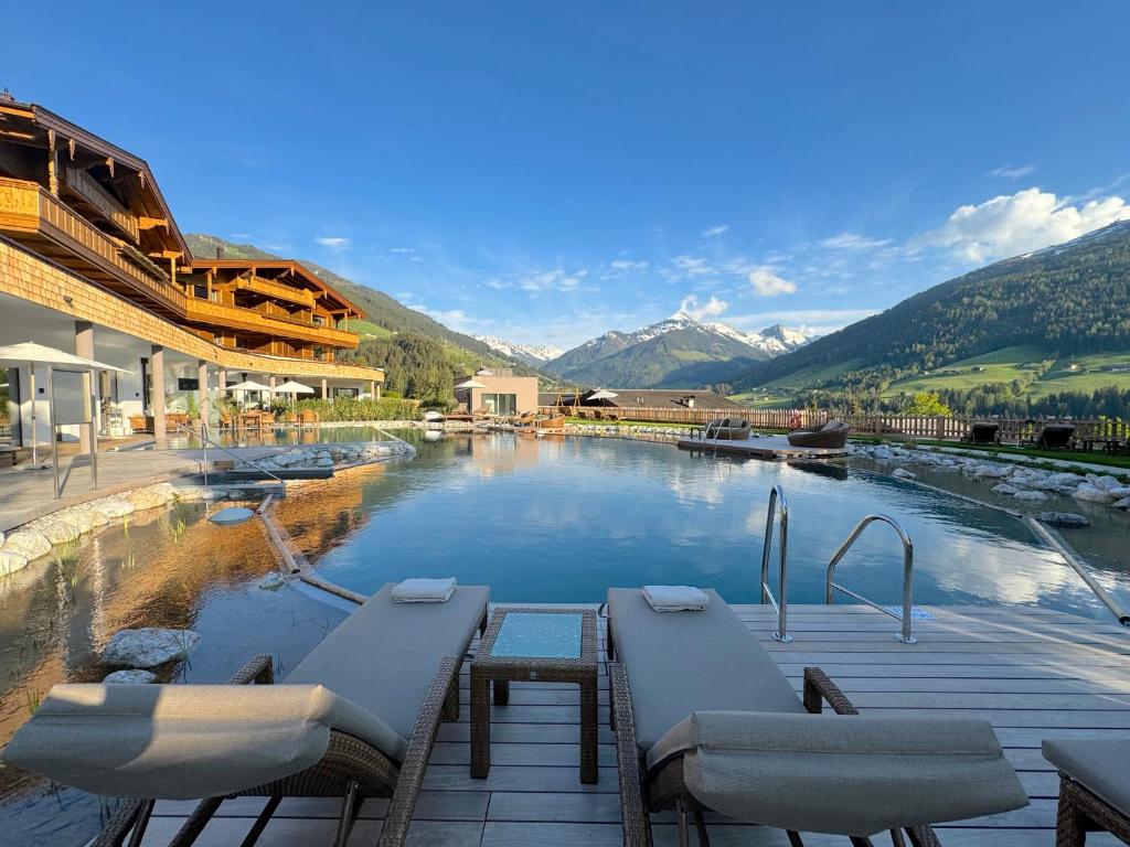a swimming pool with tables and chairs and mountains at Der Böglerhof - pure nature spa resort in Alpbach