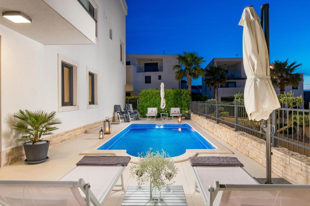 a swimming pool in a backyard with chairs and a umbrella at Luxury apartment Hyperion with private pool and garden in Murter