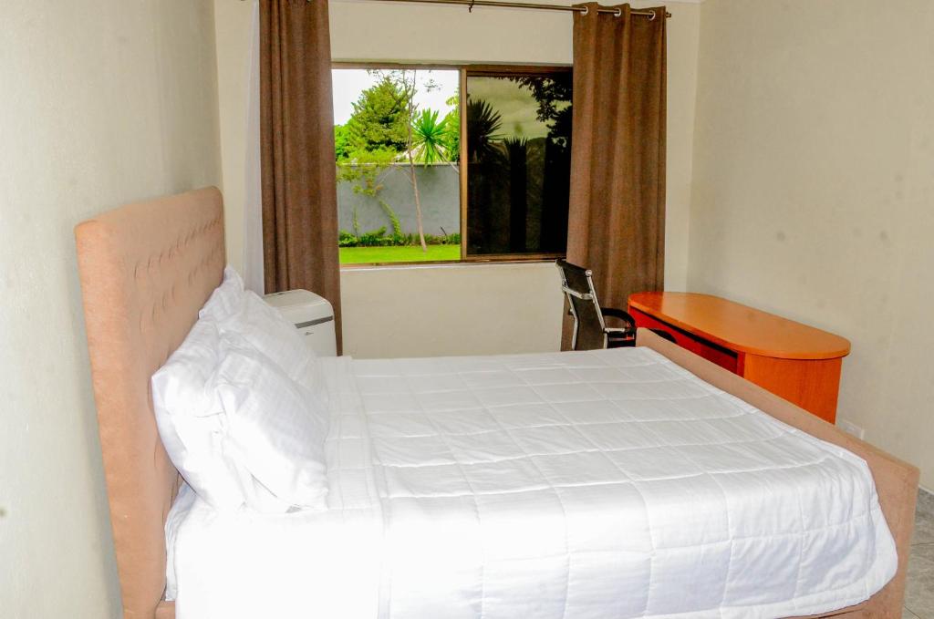 a bedroom with a bed and a desk and a window at The47 Cozy Cottage in Lilongwe