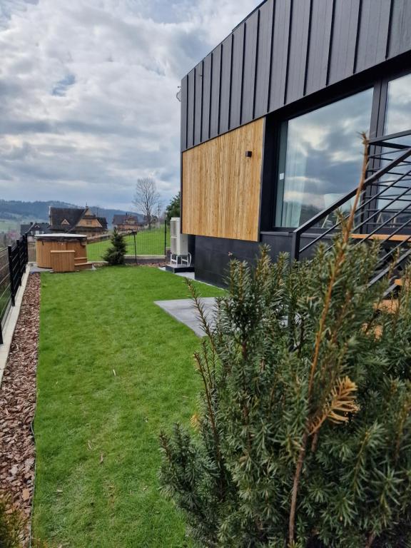 Narrow backyard beside modern home with green lawn, shrubs, stairs and outdoor hot tub in distance.