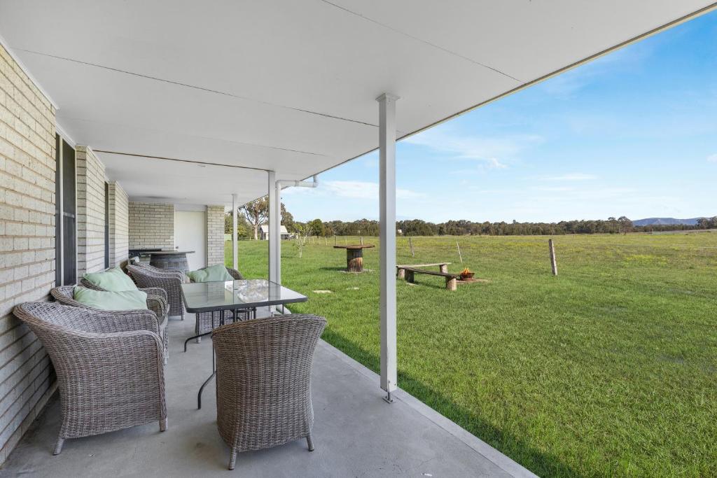 un patio con mesa, sillas y un campo en Madigan Cottages - The Homestead, en Lovedale