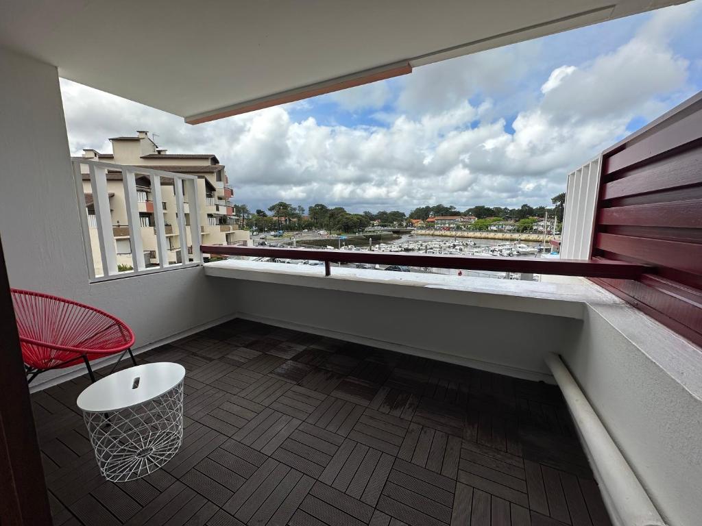 Elle comprend un balcon avec une chaise rouge et une grande fenêtre. dans l'établissement Le Bonamour sur le port de Capbreton, à Capbreton