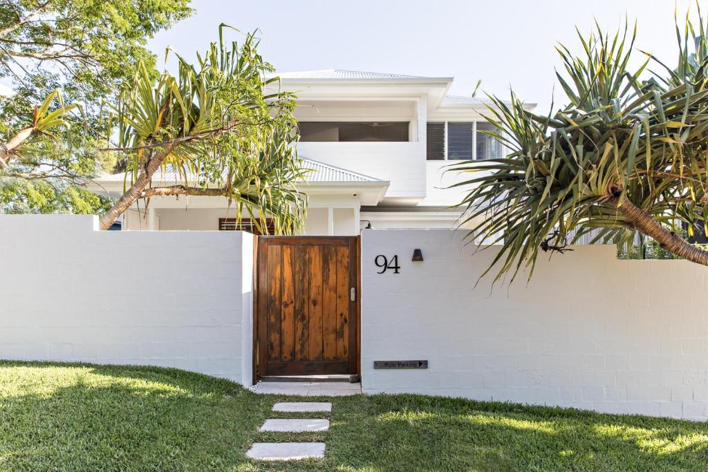 a white fence with a wooden door in front of a house at Cape Beach House in Byron Bay