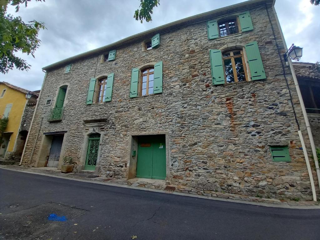 an old stone building with green doors and windows at L&#39;Armandière, maison de caractère où règne calme et sérénité. in Pézenes-les-Mines