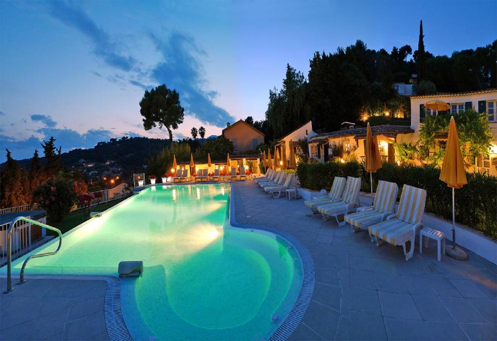 a large swimming pool with chairs and umbrellas at night at Le Hameau in Saint-Paul-de-Vence