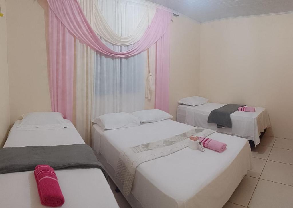 a room with three beds and a window with pink curtains at MACEDO HOSPEDAGEM in Mateiros