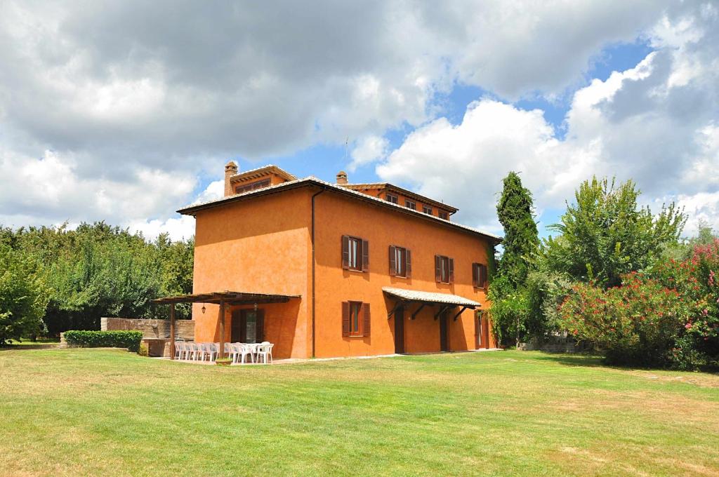 a large orange building with a grass field in front of it at Villa i Noccioli - 18 posti letto, piscina, parco in Capranica