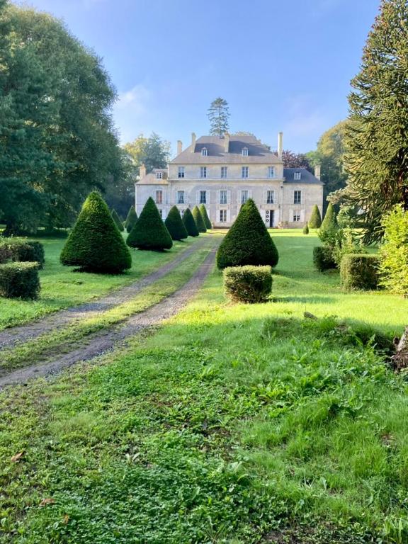 une grande maison avec une rangée d'arbres dans la cour dans l'établissement Château de Goville, à Le Breuil-en-Bessin