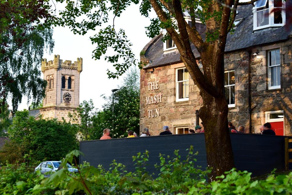 a building with a clock tower and a building with people at The Mash Tun in Aberlour