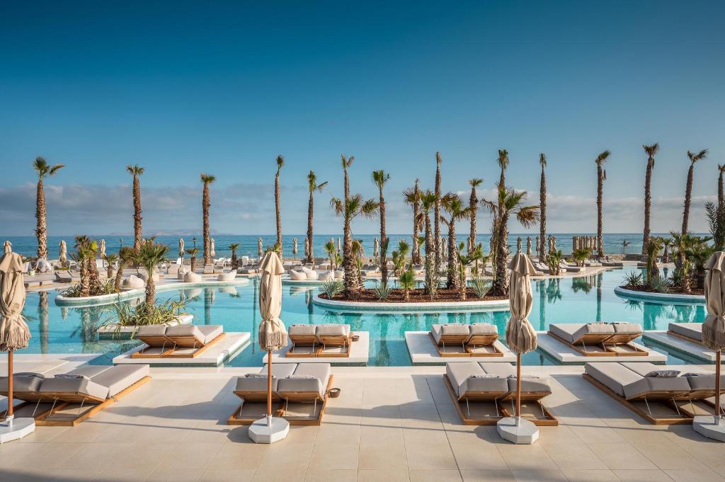 a hotel pool with chaise lounges and palm trees at Europa Beach Hotel & Spa in Hersonissos