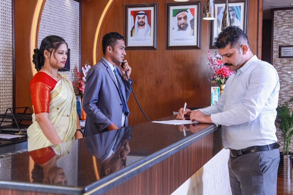 two men and a woman standing at a reception desk at Fortune Pearl Hotel in Dubai
