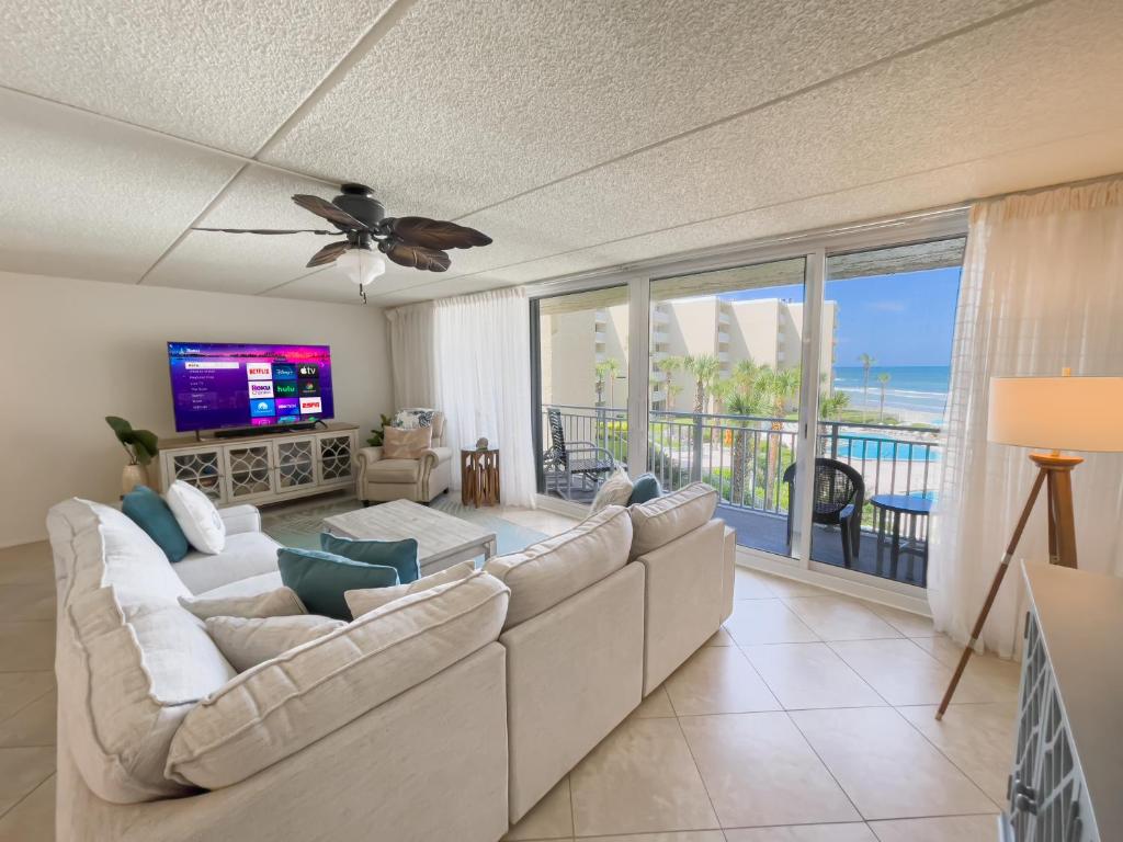a living room with a large couch and a television at Coastal condo with beachfront views and pool access! in New Smyrna Beach