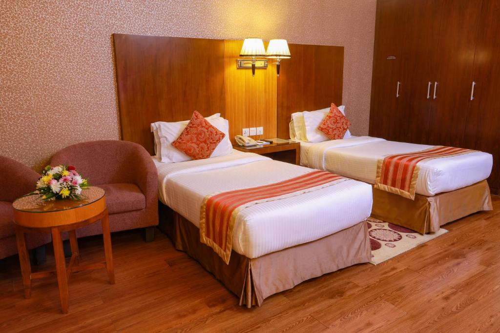 a hotel room with two beds and a chair at Fortune Pearl Hotel in Dubai