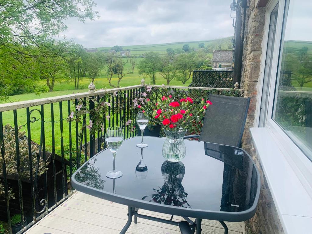 a glass table with wine glasses and flowers on a balcony at Tilly Cottage - overlooking Pendle Hill in Barrowford